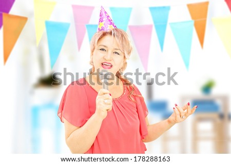 Mature lady with party hat singing on microphone at a birthday party