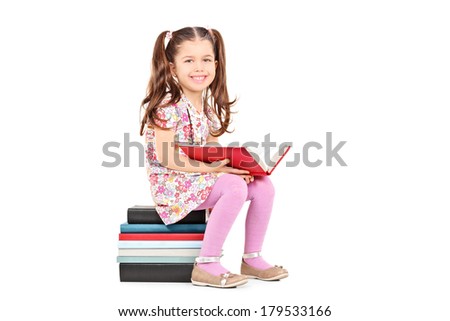 Little girl posing seated on a stack of books isolated on white background