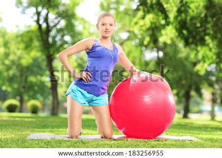 Smiling blond female posing with a pilates ball in park