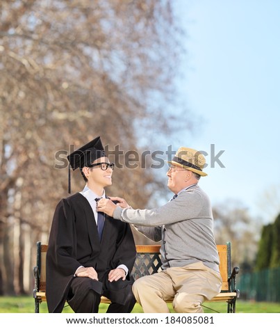 Graduate student and his proud father sitting on a wooden bench in park shot with tilt and shift lens