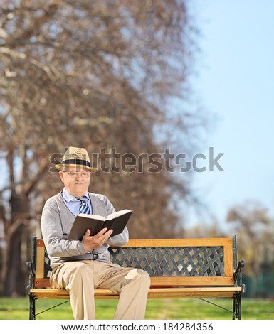 Senior sitting on bench and reading a book in park shot with tilt and shift lens