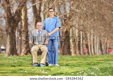 Man in a wheelchair and male nurse posing in park on a sunny day