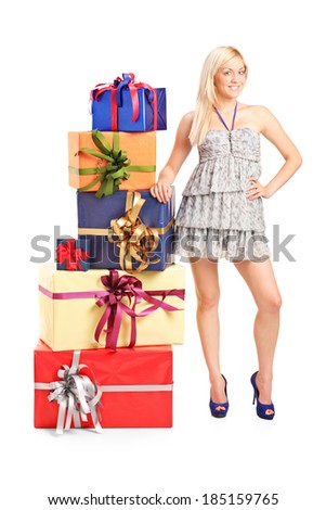 Full length portrait of an attractive girl standing next to a stack of gifts isolated on white background