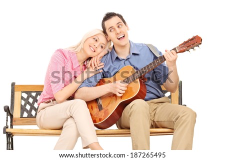 Young guy playing guitar to his girlfriend seated on bench isolated on white background