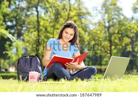 Girl sitting on grass and writing in a notebook outdoors