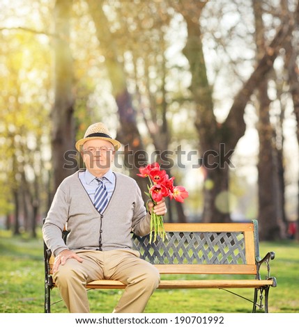 Senior man posing in park with red tulips seated on bench shot with tilt and shift lens