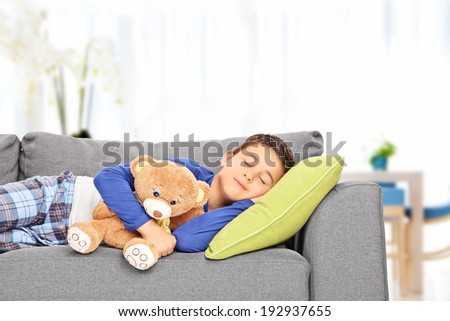 Little kid sleeping on sofa with a teddy bear indoors