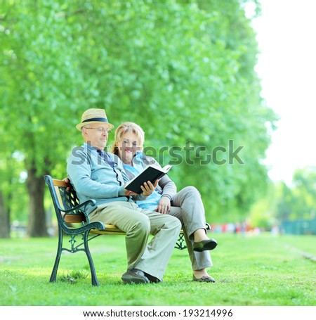 Elderly couple reading a book seated on a bench in park shot with tilt and shift lens