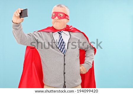 Mature man in superhero costume taking selfie on blue background