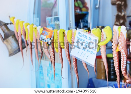 Octopus hanging on a line in front of a greek shop with note attached to the line