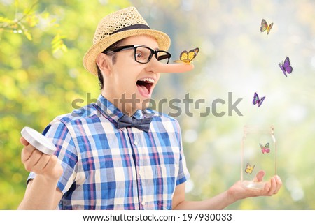 Excited man releases butterflies from jar outdoors with the focus on the one standing on his nose