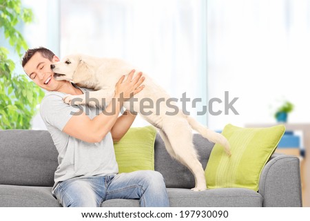 Young man playing with a puppy seated on couch at home