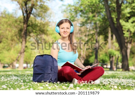 Girl studying in park and listening to a music seated in a field full of flowers