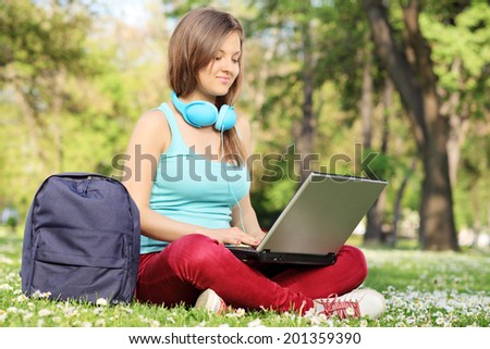 Woman studying with laptop seated on grass in park