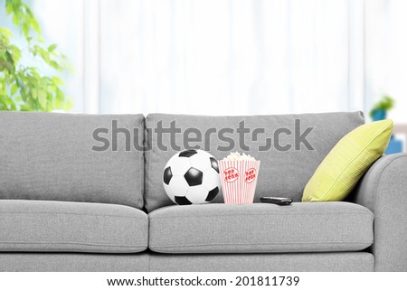 Football and a box of popcorn on a modern sofa, indoors