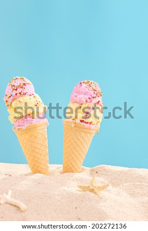 Vertical shot of two ice creams stuck in sand on blue background