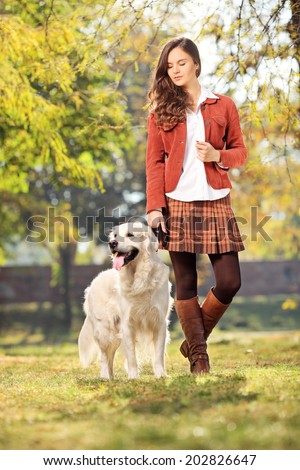 Full length portrait of a beautiful girl walking her dog in park