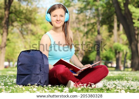 Female student reading a book in park and looking at the camera