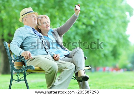 Elderly couple taking a selfie in the park seated on a bench