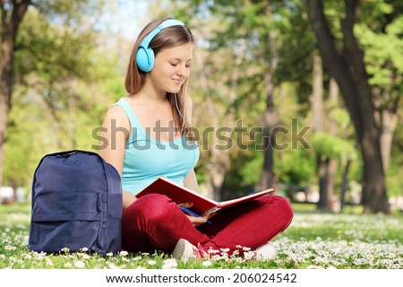Woman with headphones studying in park seated on the grass