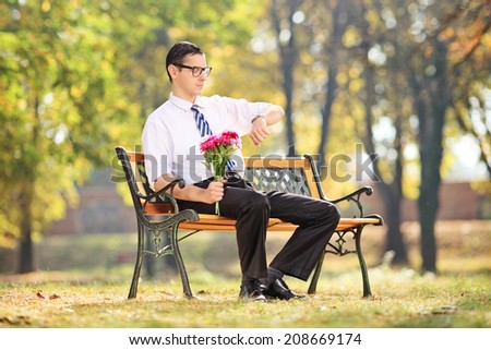 Young guy waiting for his date seated on bench in park