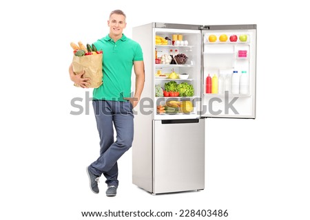 Man holding grocery bag and standing by an open fridge isolated on white background