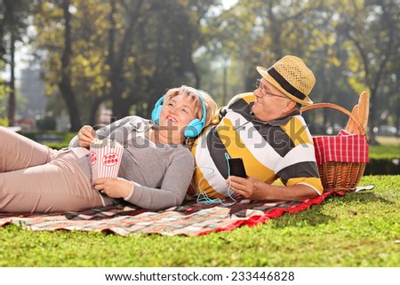 Mature couple listening music on headphones in park on a sunny day