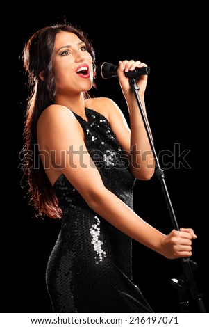 Vertical shot of a beautiful female singer singing into a microphone on black background