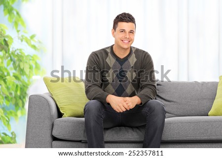 Young man posing seated on a sofa at home
