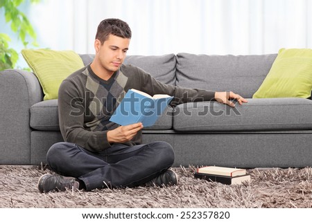 Young man reading a book seated on the floor at home