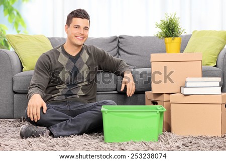 Man seated on the floor by a bunch of boxes at home