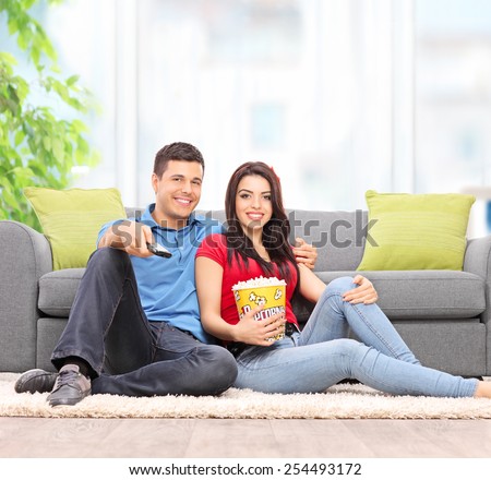 Young couple watching TV seated on the floor at home shot with a tilt and shift lens