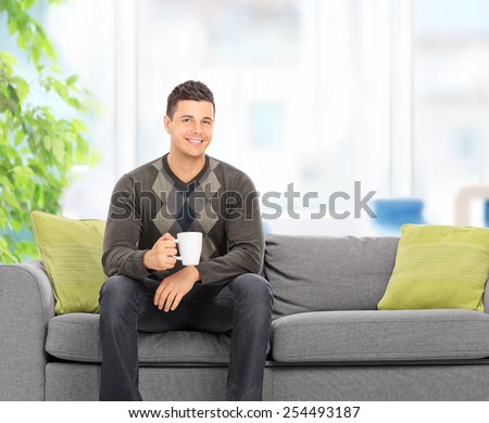 Young man drinking coffee seated on couch at home shot with tilt and shift lens