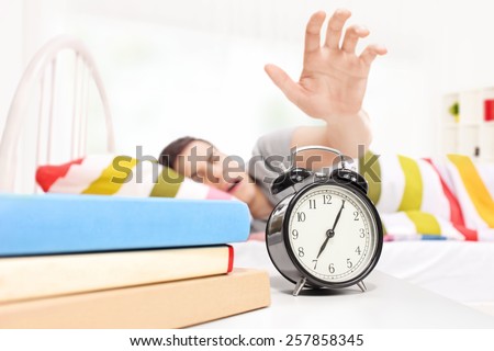 Sleepy man reaching for the alarm clock seeping on a bed at home