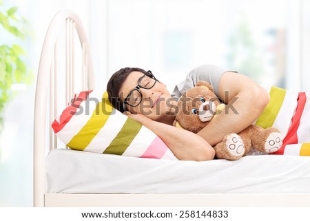 Childish young man sleeping with a teddy bear at home
