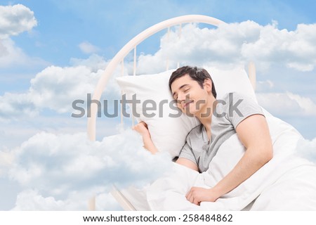 Joyful man sleeping on a bed in the clouds