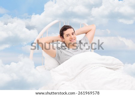 Young man relaxing on a comfortable bed in the clouds
