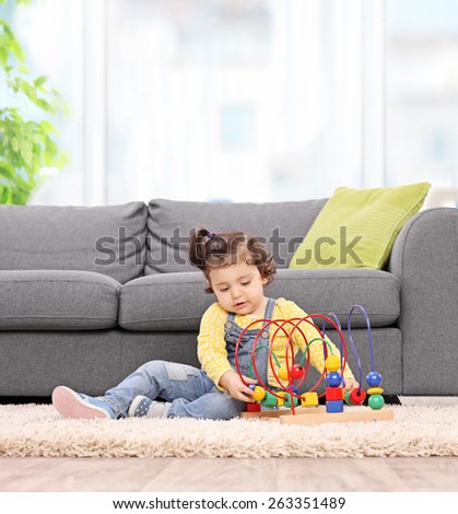 Cute baby girl playing with a logical toy seated on the floor next to a gray sofa at home. Shot with tilt and shift lens