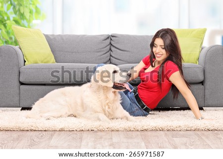 Young girl relaxing with her dog seated on the floor by a modern gray couch at home