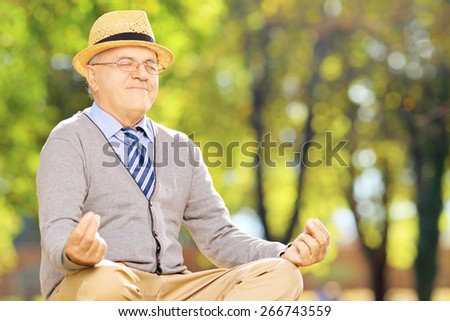 Senior gentleman meditating seated on a green grass in a park during autumn