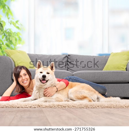 Young girl lying on the floor with her pet dog and hugging the dog by a gray couch at home shot with tilt and shift lens