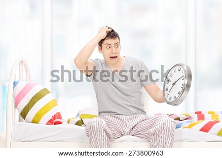 Shocked man in pajamas looking at the time in disbelief and sitting on his bed at home