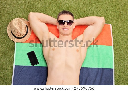 Close-up on a handsome young man lying on a towel and sunbathing in his backyard