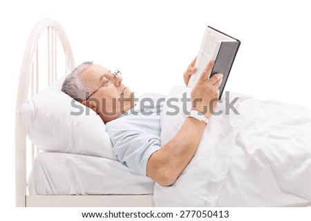 Mature patient reading a book and lying in a hospital bed covered with a white blanket isolated on white background