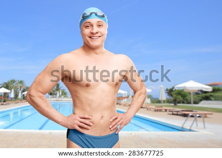 Young man with a swimming cap and goggles posing in front of a swimming pool and smiling