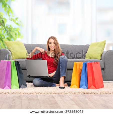 Young woman holding a laptop and sitting in front of a couch with a bunch of shopping bags around her at home shot with tilt and shift lens