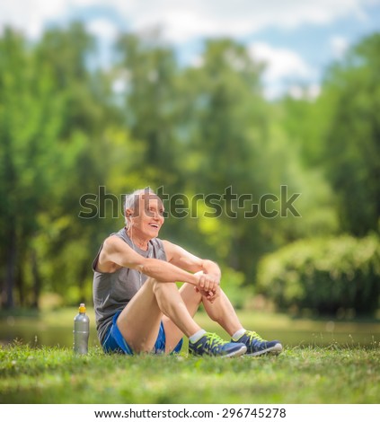 Athletic senior in sportswear sitting on grass in a park and listening to music on headphones shot with tilt and shift lens