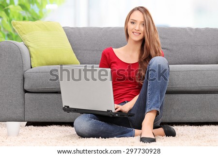 Young woman working on laptop seated on the floor at home