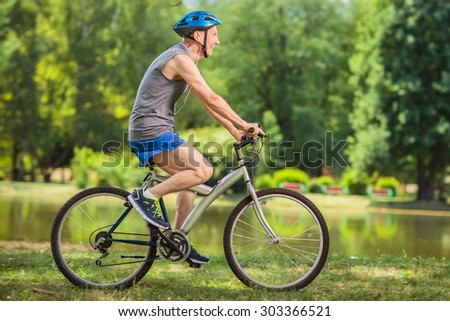 Profile shot of a joyful senior biker riding a bicycle in a park by a pond on a beautiful summer day