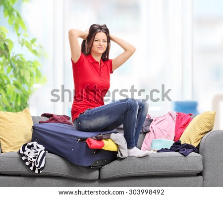 Frustrated woman sitting on a suitcase packed full of clothes and looking at the camera at home shot with tilt and shift lens